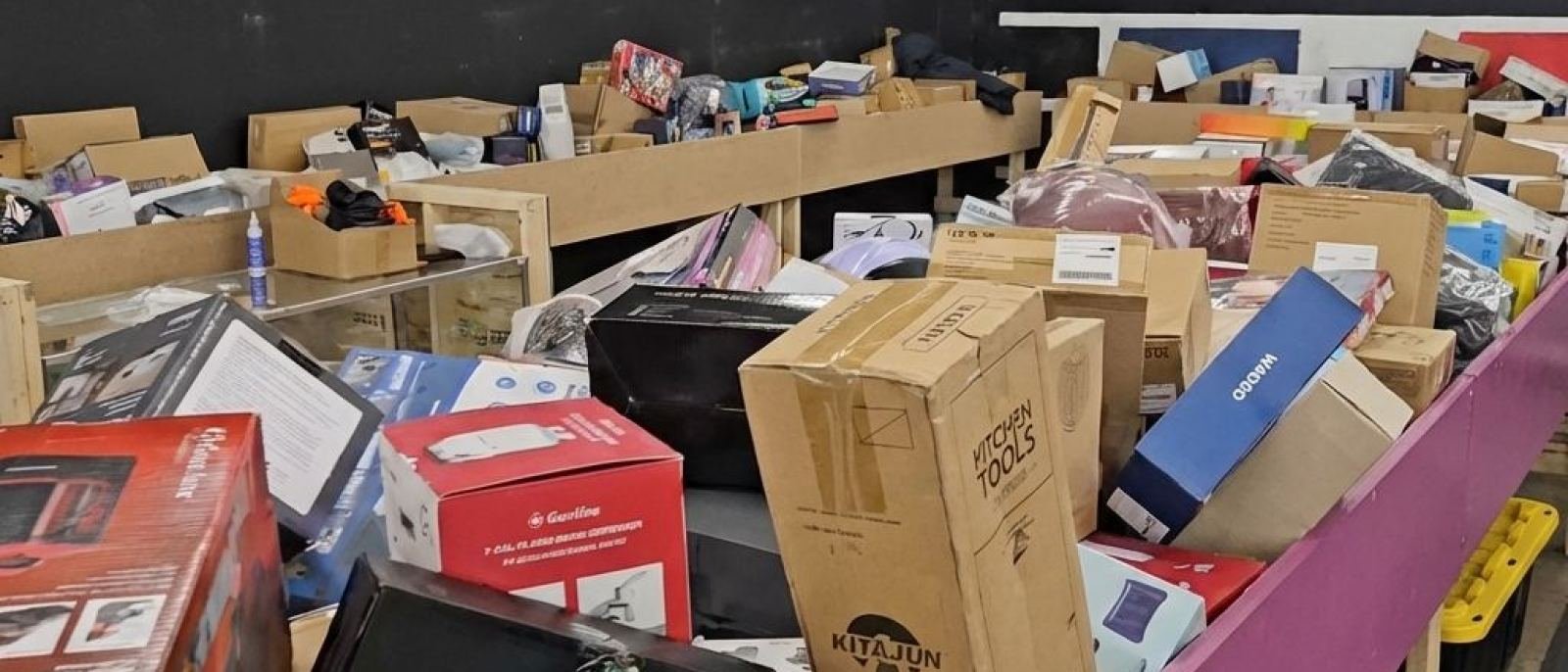Boxed electronics, kitchen appliances and tools stacked along the rail of a bin at Amazing Stock